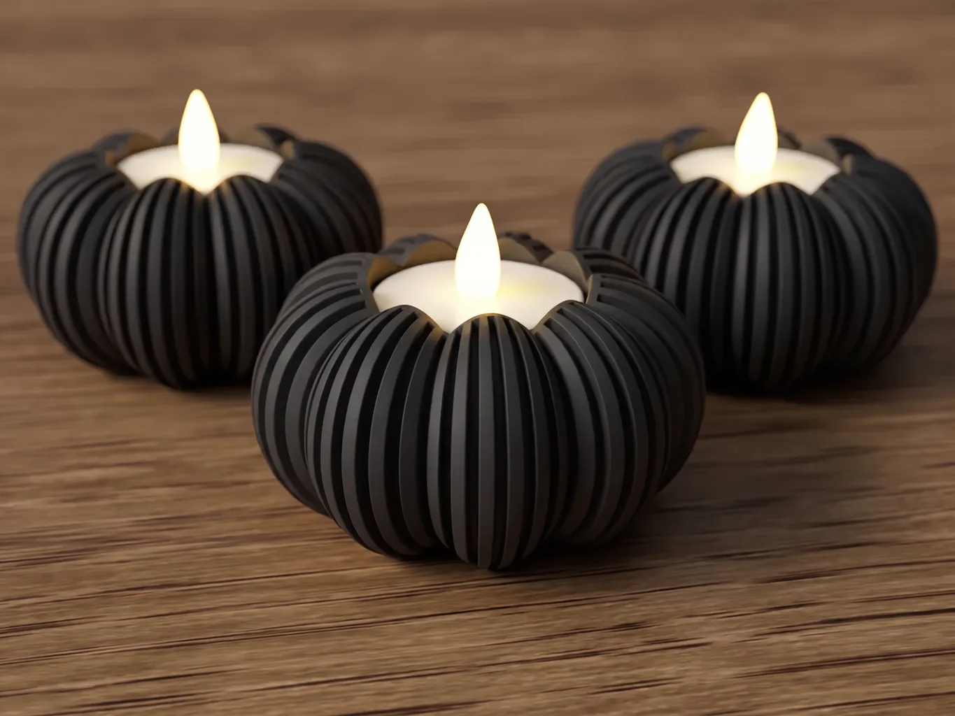 Three pumpkin-shaped 3D printed candleholders in matte black, ribbed, each filled with a lit LED candle, on a wooden table