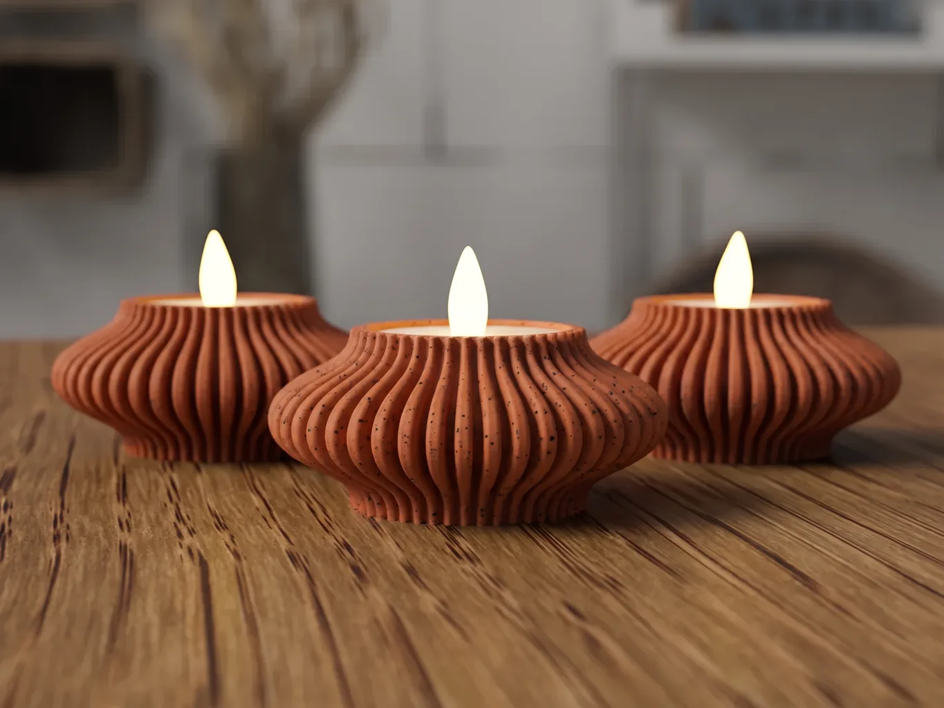 Drei 3D-gedruckte Kerzenhalter Ondéa, flache breite Schalen mit strahlenförmigen Rippen in marmoriertem Terrakotta, jede mit einer brennenden LED-Kerze, auf einem Holztisch
